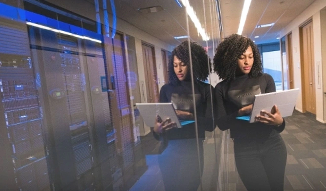 Technician with a tablet standing beside glass-enclosed server racks in a data center